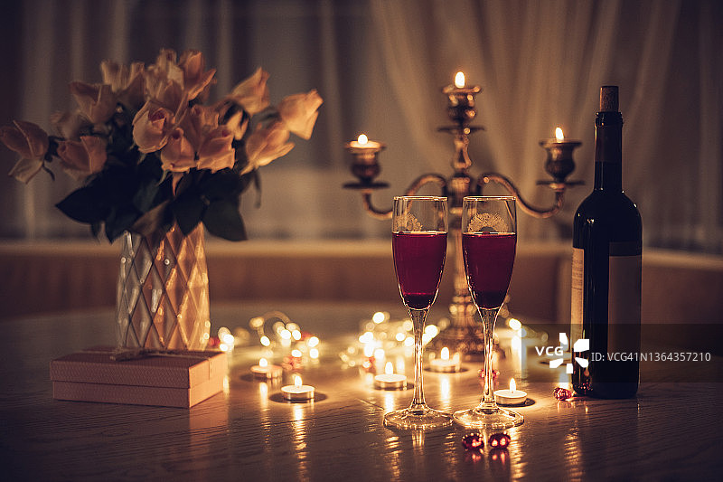 燭光日期。桌上擺著酒杯、蠟燭、玫瑰花束和禮盒。晚上在家浪漫的燭光晚餐圖片素材