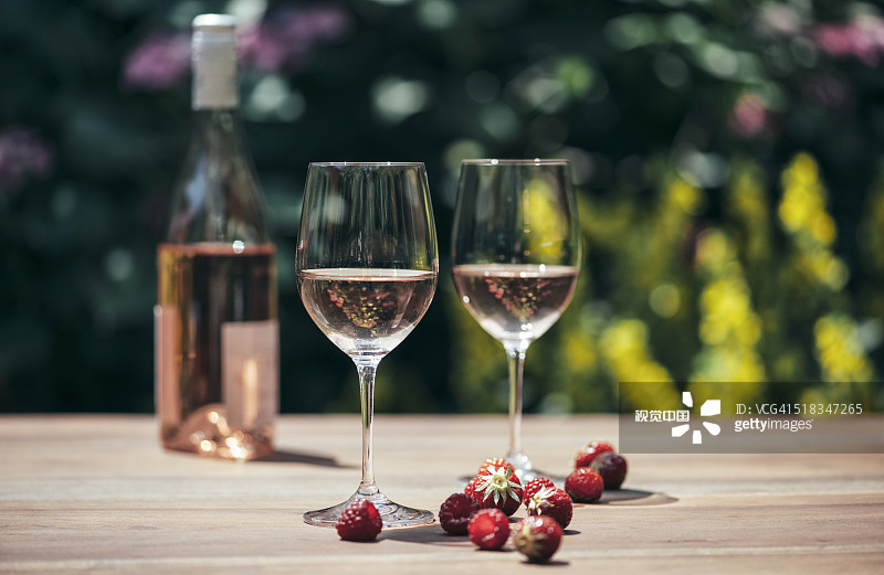 兩杯玫瑰酒，酒瓶，草莓和覆盆子放在木桌上圖片素材