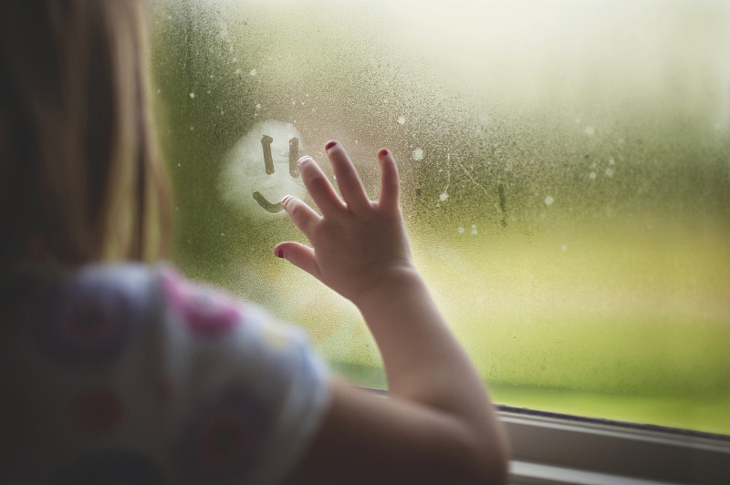 裁剪圖像的女孩做擬人化的笑臉在潮濕的窗戶在家里雨季圖片素材
