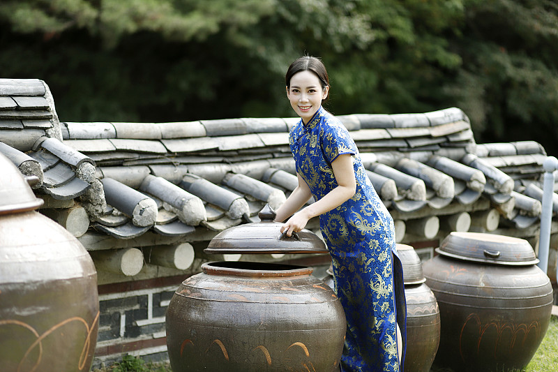穿著旗袍的女子站在長穴臺，韓國傳統的壇子旁圖片素材