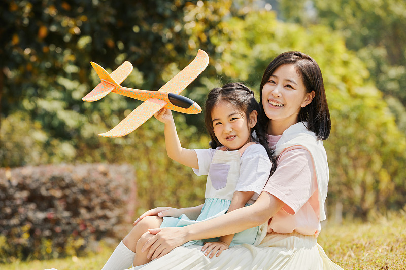 手拿飞机模型的小女孩坐在妈妈的腿上图片下载