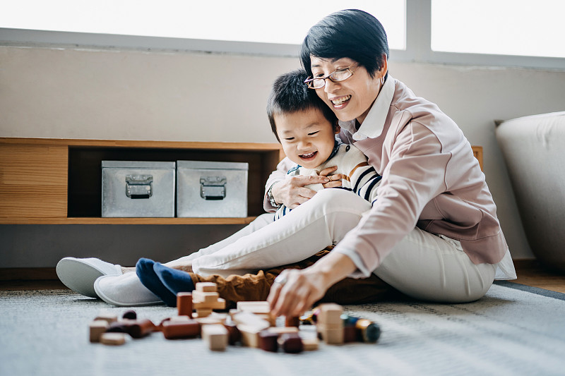 快樂的亞洲奶奶坐在客廳的地板上和小孫子一起玩積木圖片素材