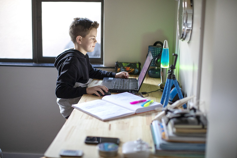 一個九歲的男孩在家里用筆記本電腦做作業。圖片素材