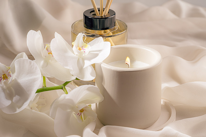 蠟燭在柔和的米色絲綢織物背景與白色蘭花和柔和的家的香味。圖片下載