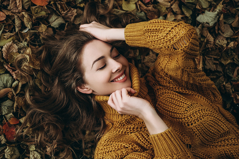 年輕女子躺在秋葉上。圖片下載