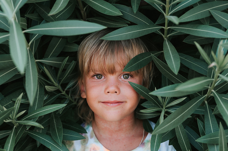 肖像的坦率快樂的小男孩的臉，五歲的問題過敏皮膚和金色的長發和綠色的眼睛，背景是綠色的植物在暑假旅行圖片素材