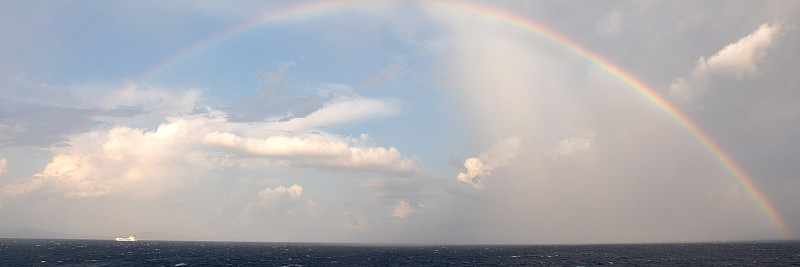 整個彩虹在海上和小船附近攝影圖片