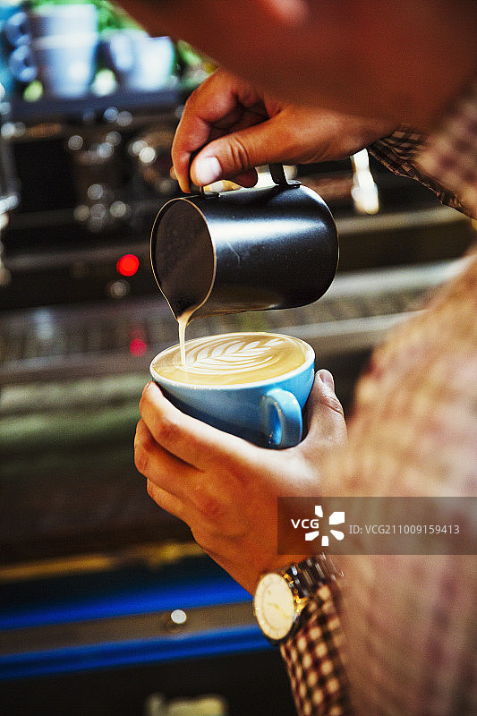 专业咖啡店。咖啡师把热牛奶倒进咖啡的泡沫里，做成一个图案。图片素材