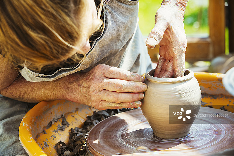 在她的作坊里，一个妇女在陶工转盘上制作陶土。图片素材