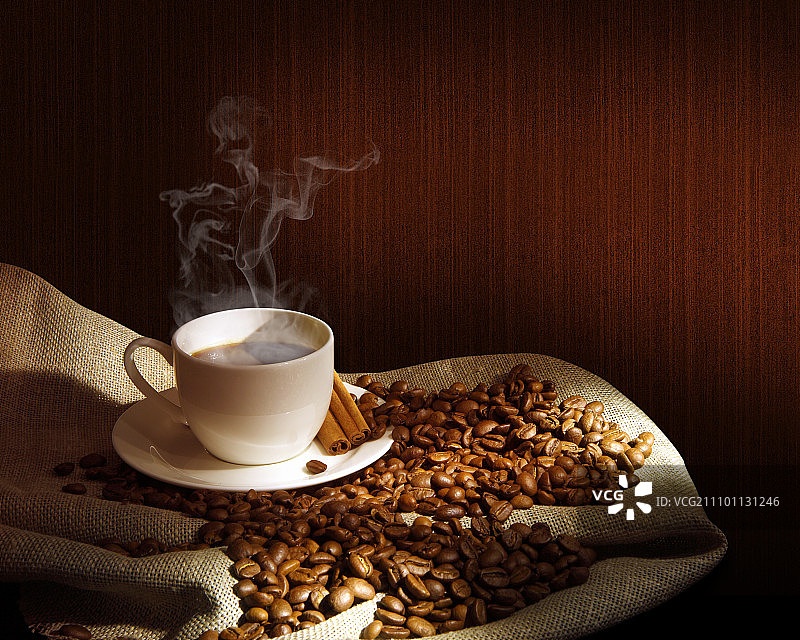 一杯热气腾腾的咖啡，肉桂棒和一些咖啡豆。静物画图片素材