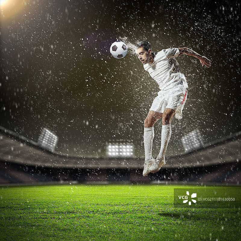 足球运动员击球。穿着白衬衫的足球运动员在雨中在体育场用头击球图片素材
