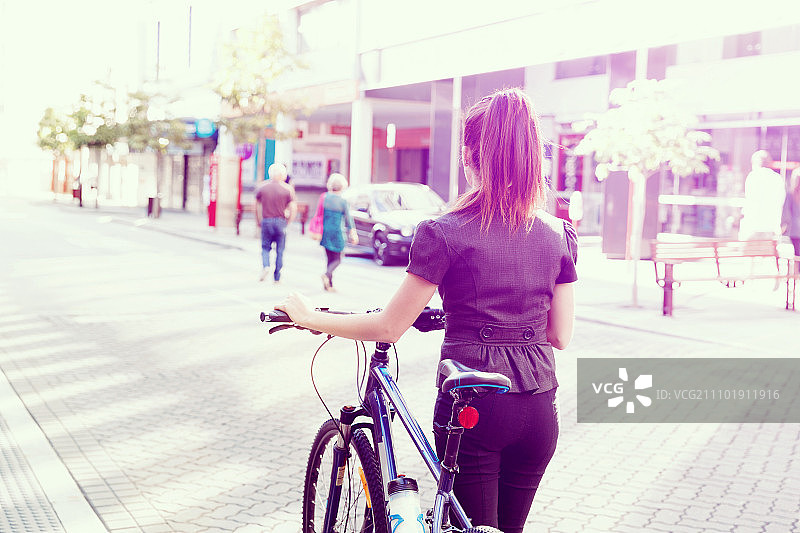 年轻女子骑自行车上下班。年轻的女商人穿着自行车在城市里通勤图片素材