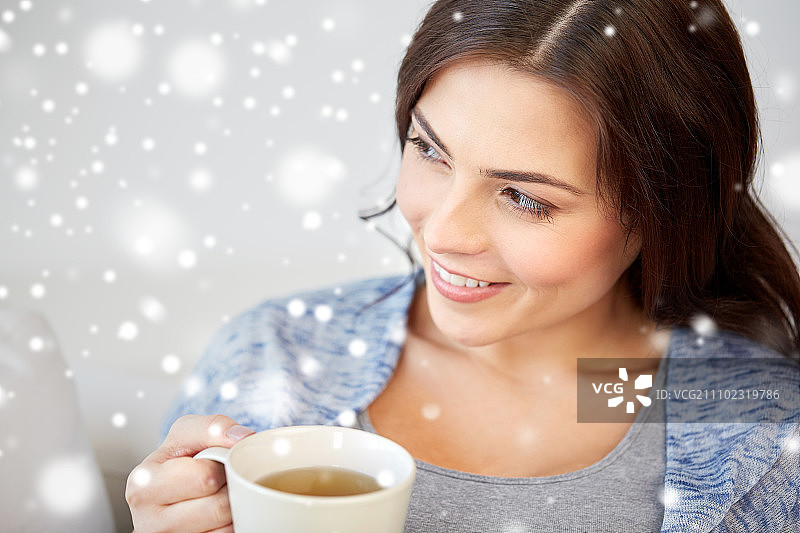 人们，饮料，圣诞和冬天的概念-快乐的年轻女子与一杯茶在家里过雪图片素材