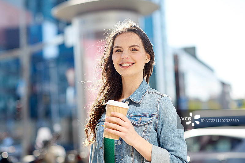 饮料和人们的概念-快乐的年轻女子或少女喝咖啡从纸杯在城市的街道。快乐的年轻女子在城市街道上喝着咖啡图片素材