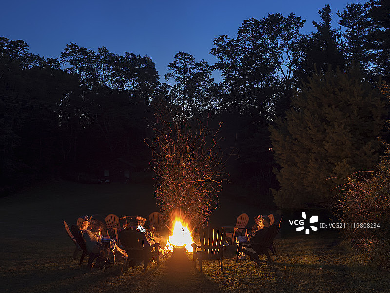 在渐浓的夜色中，人们围坐在篝火旁。图片素材