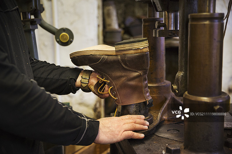 近距离的工人在一个鞋匠的车间，使用一台机器制作皮革踝靴。图片素材