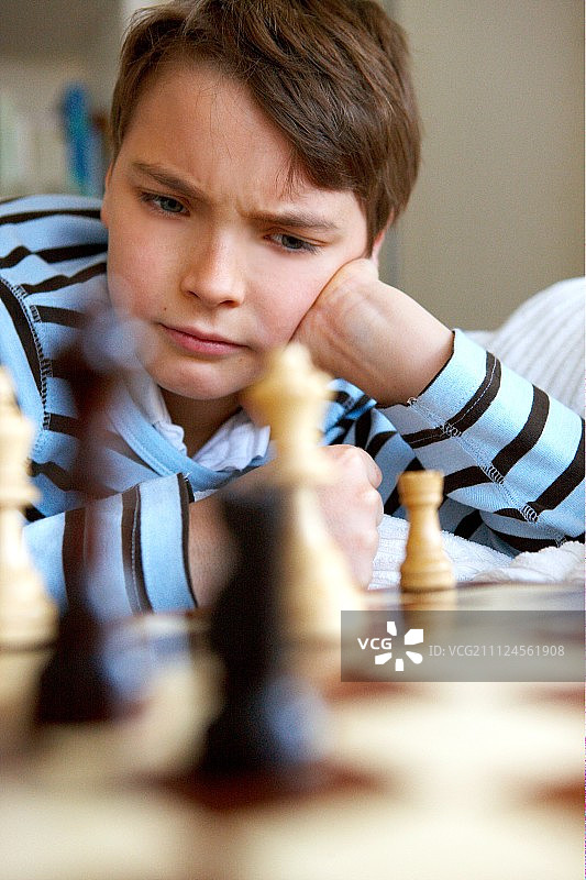 沉思的男孩穿着条纹毛衣坐着下棋图片素材