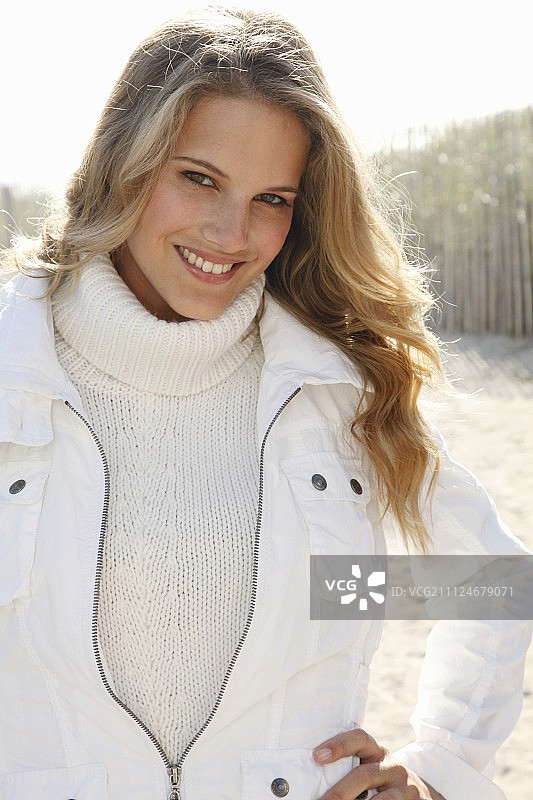 一个年轻的金发女人穿着白色夹克外的白色针织翻领套头衫图片素材