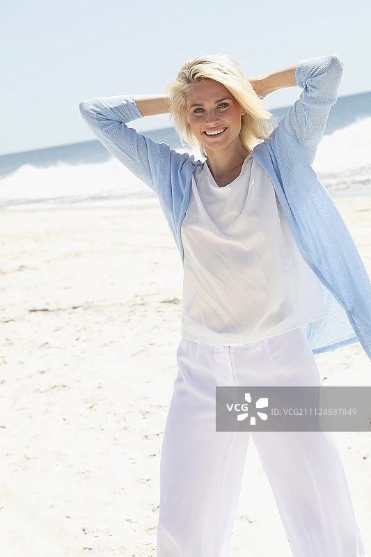 一个金发女人在海滩上穿着白色衬衫，裤子和浅蓝色开襟羊毛衫图片素材
