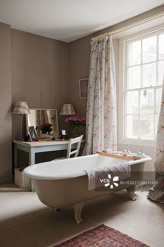 独立的老式浴缸在窗前，长及地板的窗帘和梳妆台与镜子在房间的角落图片素材