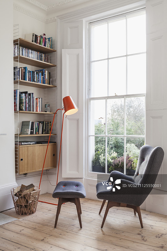 大格子窗旁舒适的阅读角，灰色复古的靠背椅搭配脚凳，橙色标准灯和壁龛内的书柜图片素材