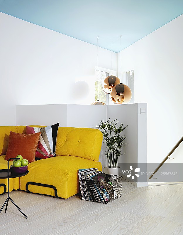 黄色沙发，靠垫，铁丝筐，黑色金属边桌，背景是半高的白色栏杆和楼梯，淡蓝色天花板上挂着吊灯图片素材