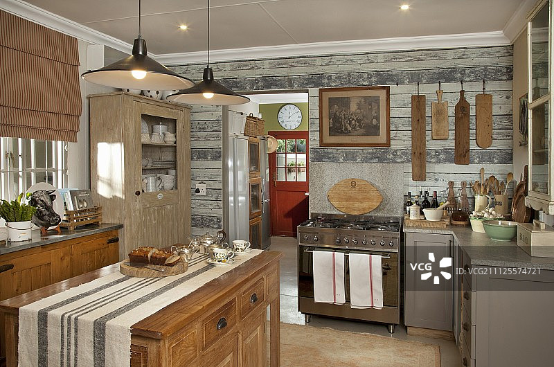 乡村风格的厨房，独立的实木岛式柜台，下面是带有金属灯罩的吊灯图片素材