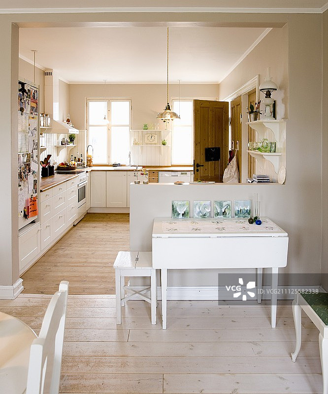 从用餐区可以看到开放式的乡村厨房，白色折叠桌靠在半高的隔断上图片素材