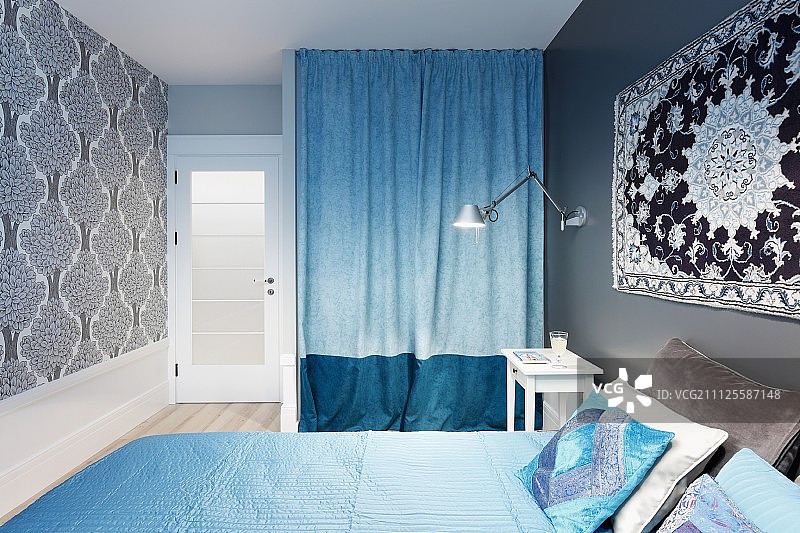 双人床上面的墙上挂着一块地毯，上面有浅蓝色的床罩，壁龛里有两种色调的蓝色窗帘图片素材
