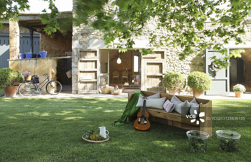 吉他放在花园的木凳上，石头房子外面有开放的露台门图片素材