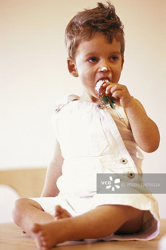 小男孩坐在桌子上，吃着草莓和奶油图片素材