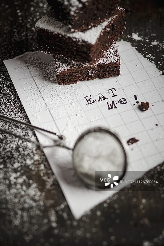三块巧克力饼叠在一张写着“吃我”的白纸上图片素材