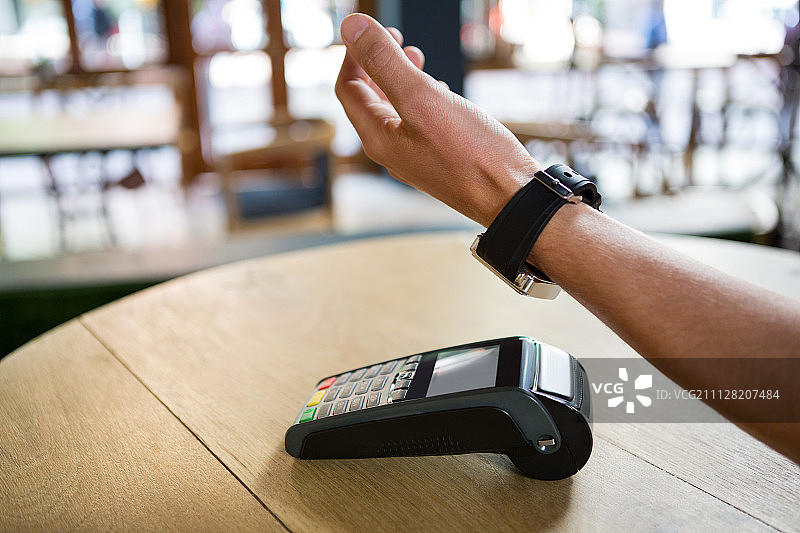 裁剪图像的人的手使用智能手表表达支付在咖啡店图片素材