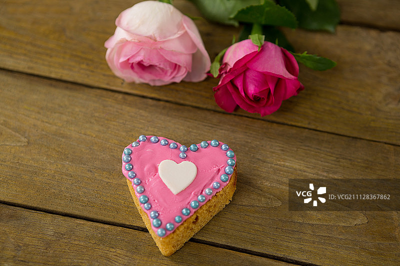 特写的粉色玫瑰与心形饼干在木板上图片素材