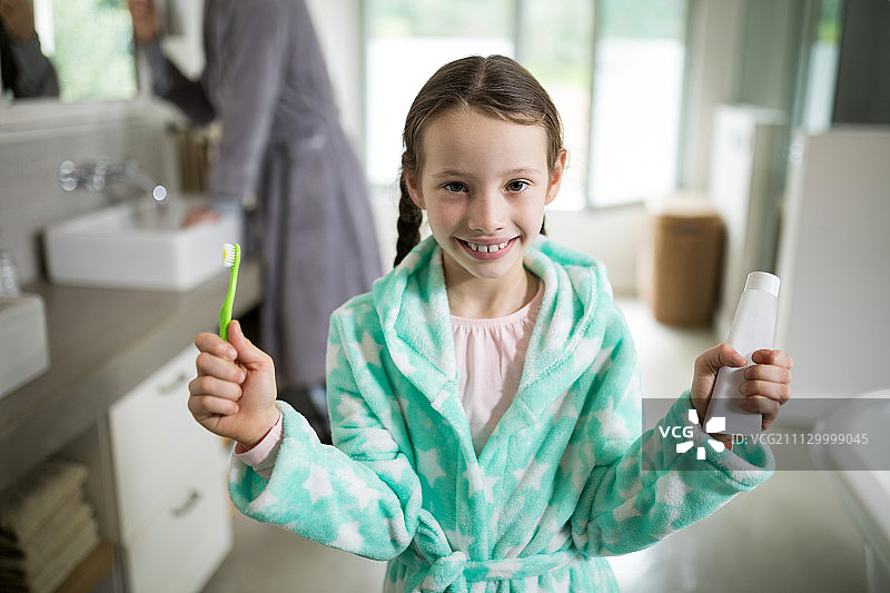 一个微笑的女孩在浴室里拿着牙膏和牙刷图片素材