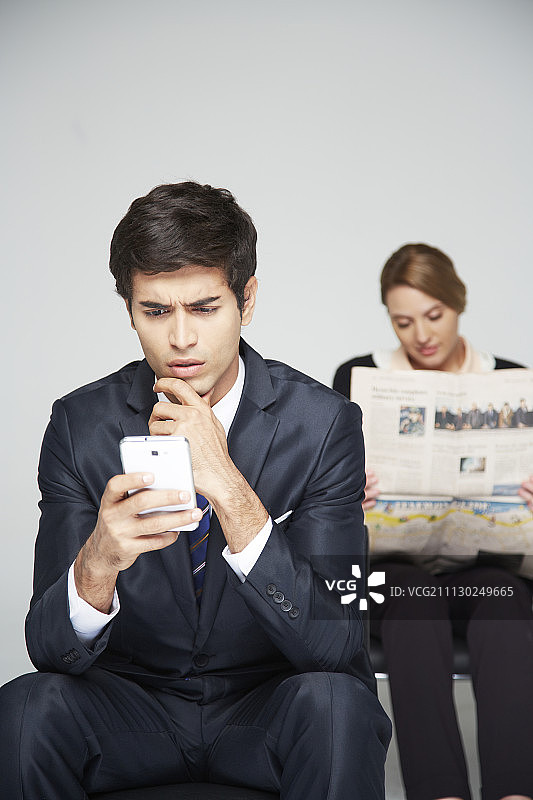 商人正在看他的智能手机和女商人正在看背后的报纸图片素材