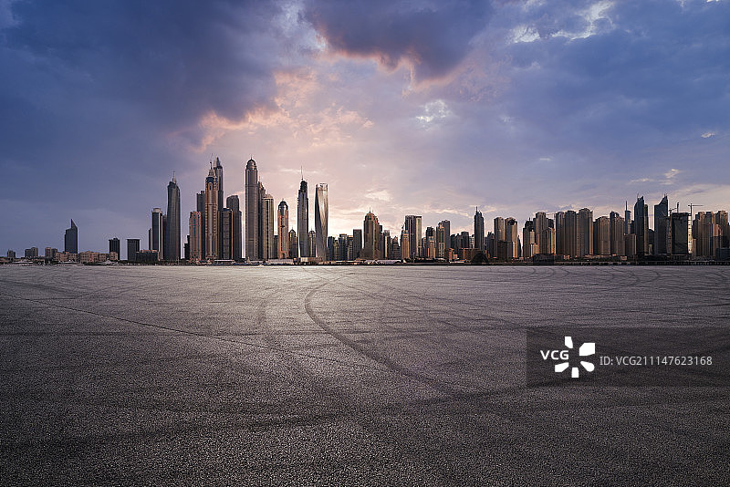 逆光下的迪拜摩天大楼和布满轮胎印的试车跑道广场图片素材