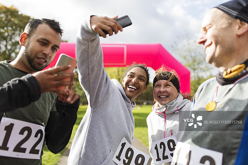 快乐的跑步者朋友们在公园的慈善跑步中用照相手机自拍图片素材