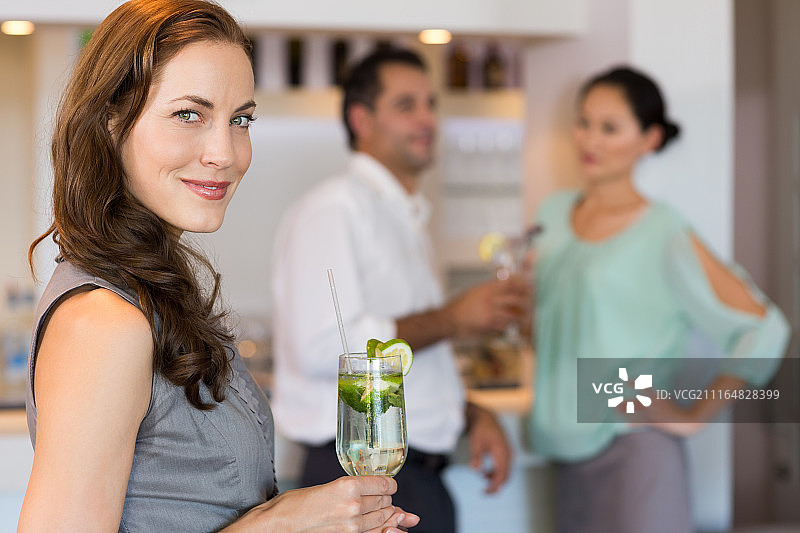 微笑的女人拿着鸡尾酒杯和朋友在后面的酒吧图片素材