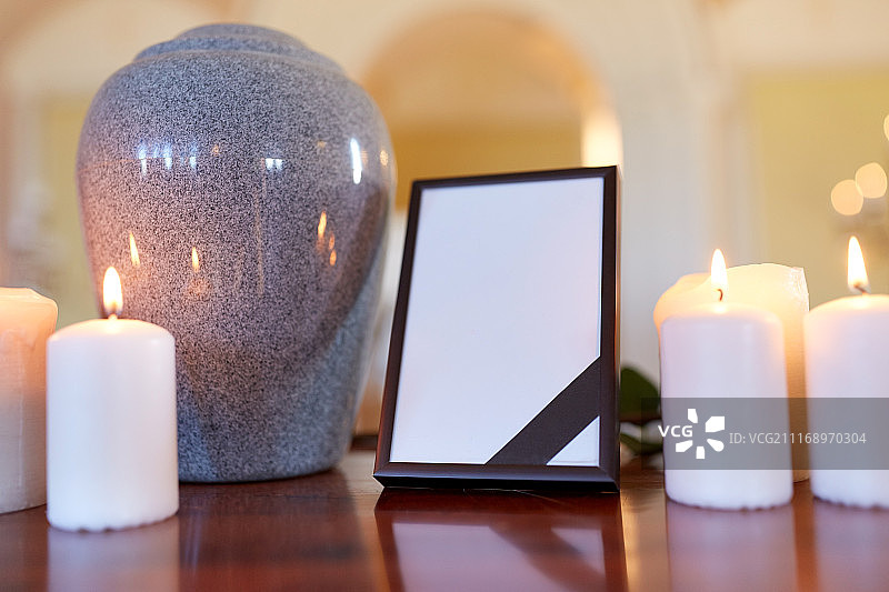 葬礼和悼念概念-相框黑色丝带，火葬缸和燃烧的蜡烛在教堂的桌子上。相框，火葬缸和教堂里的蜡烛图片素材