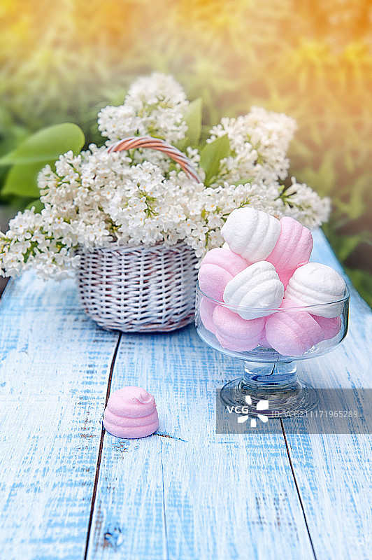 白色和粉红色的棉花糖在圆形玻璃花瓶和一篮精致的白色紫丁香。…图片素材