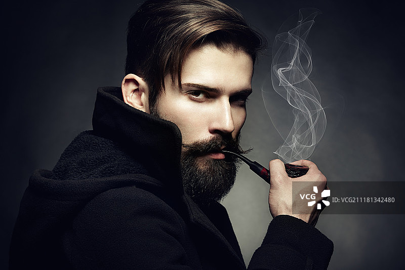 年轻漂亮的男人的黑色艺术肖像。那个年轻人抽烟斗。近距离图片素材