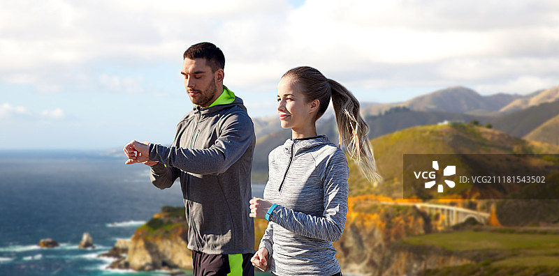 健身，运动和健康的生活方式的概念-微笑的夫妇与心率手表跑过比克斯比溪桥在大海岸的加利福尼亚背景。配上健身追踪器在户外跑步。配上健身追踪器在户外跑步图片素材