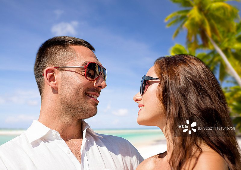 旅游，旅游和夏季度假概念-幸福的微笑夫妇在太阳镜在法国波利尼西亚的热带海滩背景。在热带海滩上，一对戴着太阳镜的幸福夫妇。在热带海滩上，一对戴着太阳镜的幸福夫妇图片素材