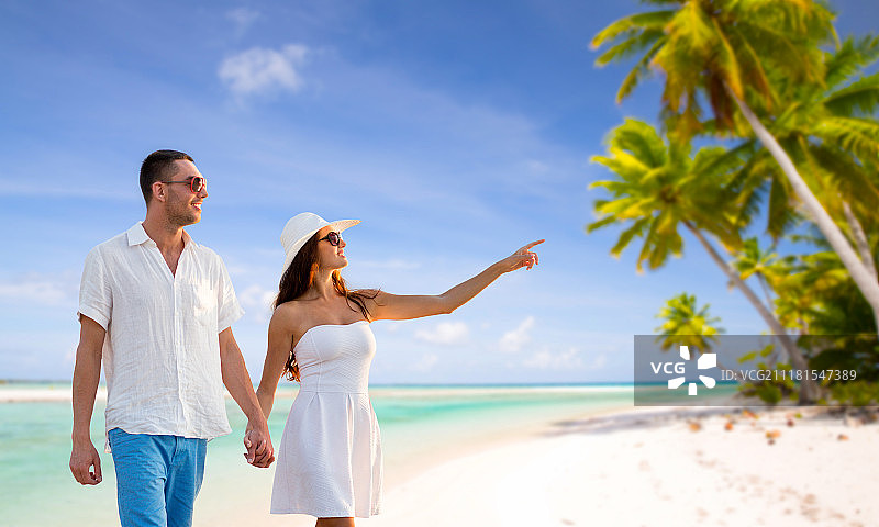旅游，旅游和夏季度假概念-幸福的夫妇度假戴着太阳镜，手牵着手走过热带海滩背景在法属波利尼西亚。一对在热带海滩度假的幸福夫妇。一对在热带海滩度假的幸福夫妇图片素材