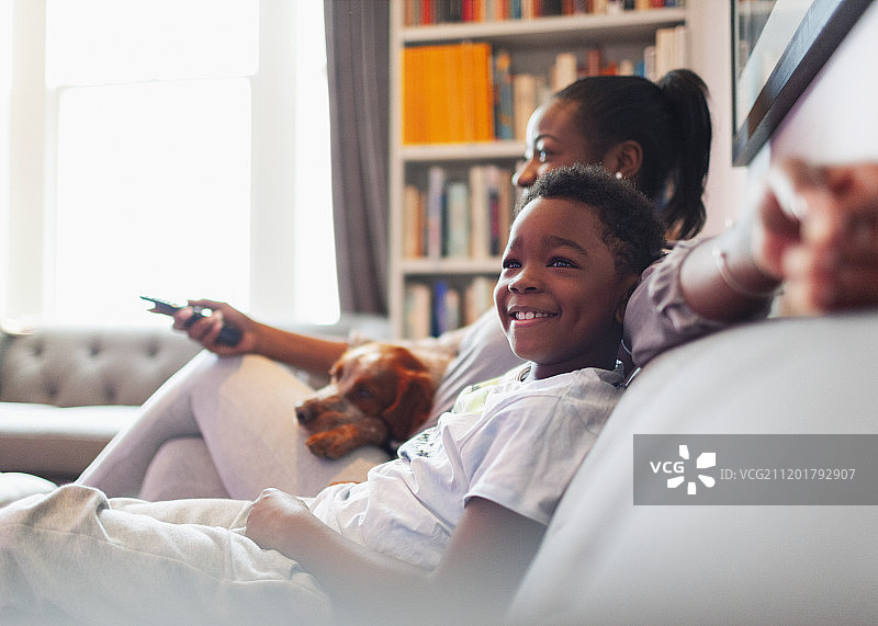 快乐的男孩和妈妈和狗在客厅的沙发上看电视图片素材