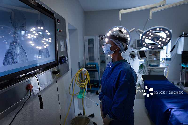 一位白种女外科医生在手术室里看着手术监视器的侧视图图片素材
