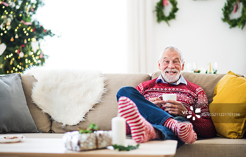 一位老人坐在家里的沙发上喝着咖啡。图片素材
