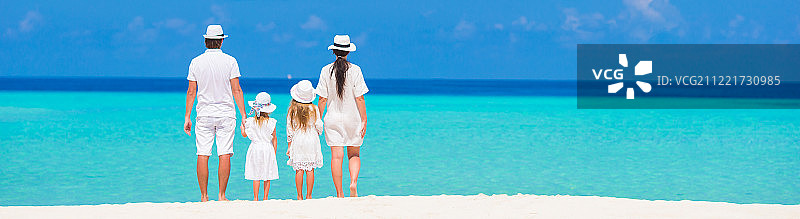 后视图年轻美丽的家庭在白色热带海滩图片素材