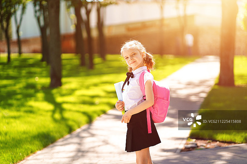 美丽的小女孩背着背包在公园里散步准备回学校图片素材